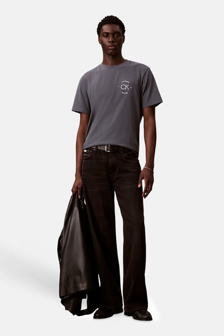 T-shirt gris à manches courtes de Calvin Klein, avec logo imprimé, porté avec un pantalon noir et une veste.