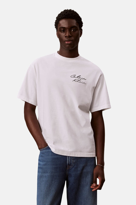 T-shirt blanc à manches courtes de Calvin Klein, avec logo noir brodé sur le devant, porté avec un jean bleu.
