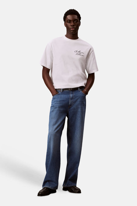 T-shirt blanc à manches courtes de Calvin Klein, porté avec un jean bleu et des mocassins noirs.