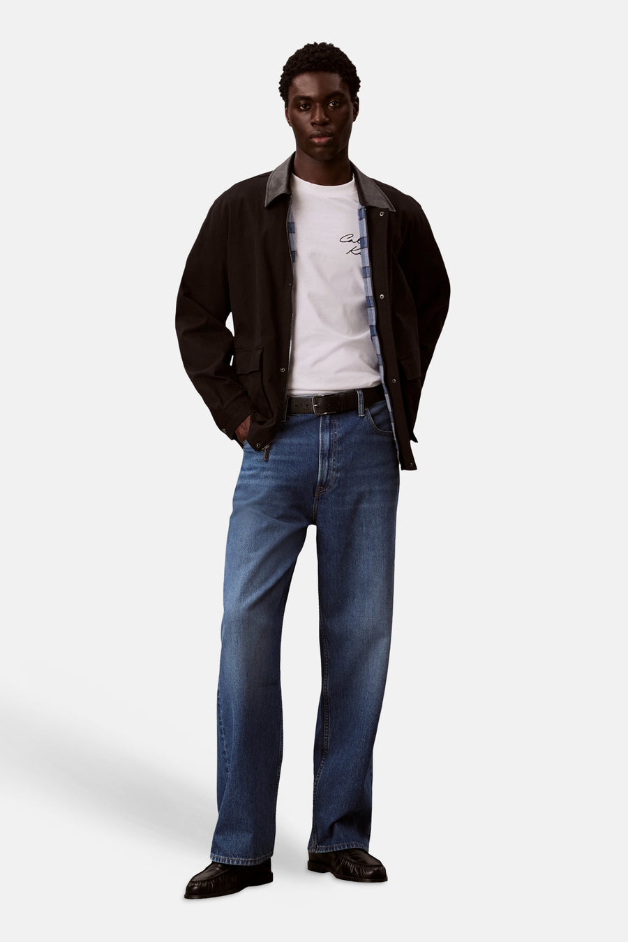 T-shirt blanc à manches courtes de Calvin Klein, porté sous une veste marron et une chemise à carreaux.
