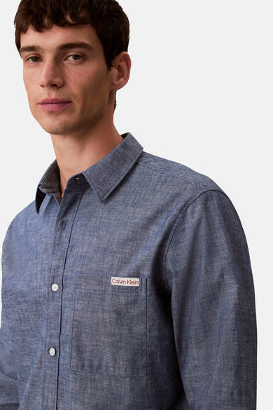 Chemise à manches longues bleue de Calvin Klein, avec poche poitrine et boutons blancs, sur fond uni.