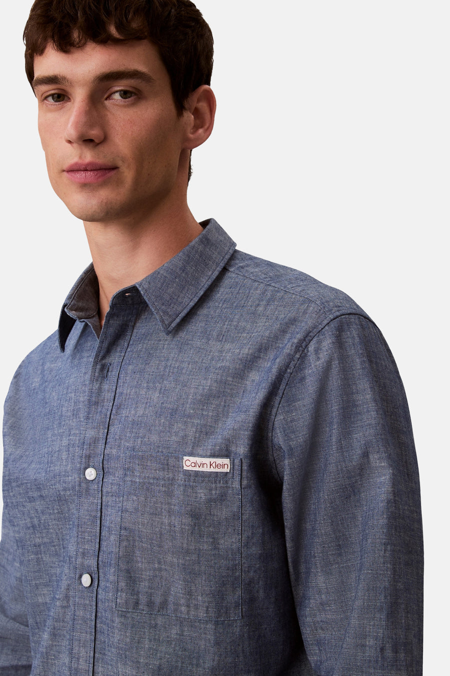 Chemise à manches longues bleue de Calvin Klein, avec poche poitrine et boutons blancs, sur fond uni.