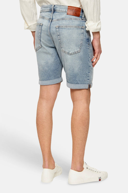 Short en jeans bleu clair de Calvin Klein, avec chemise et baskets blanches, vue arrière.