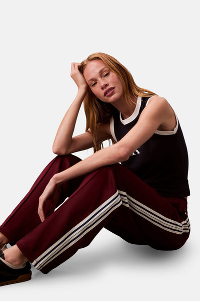 Bordeaux joggingbroek van Calvin Klein, met drie witte strepen aan de zijkant, gedragen met een zwarte tanktop.