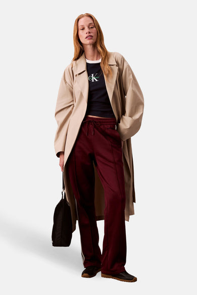 Bordeaux joggingbroek van Calvin Klein met witte strepen aan de zijkant, gedragen met een beige trenchcoat.