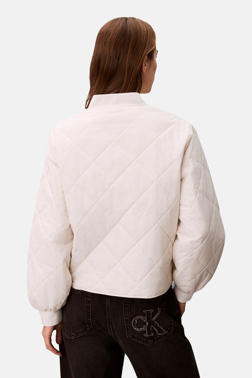 Veste courte écru de Calvin Klein avec motif matelassé en losanges, portée avec un jean noir logo CK sur la poche arrière.