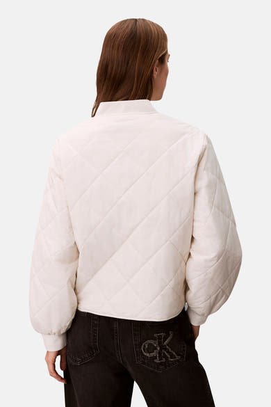 Veste courte écru de Calvin Klein avec motif matelassé en losanges, portée avec un jean noir logo CK sur la poche arrière.