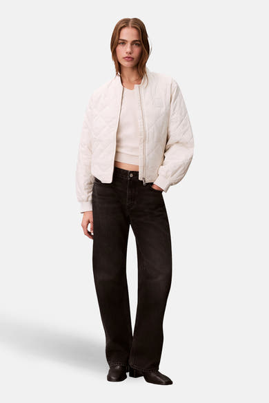 Korte gebroken witte Calvin Klein jas, gewatteerd met ritssluiting en gedragen met een zwarte jeans.