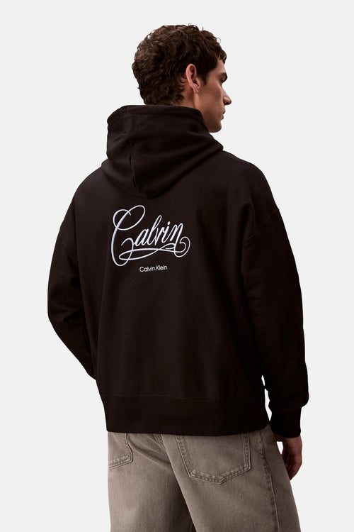 Zwarte Calvin Klein hoodie met trekkoord en discreet logo op de borst, gedragen met een grijze jeans.