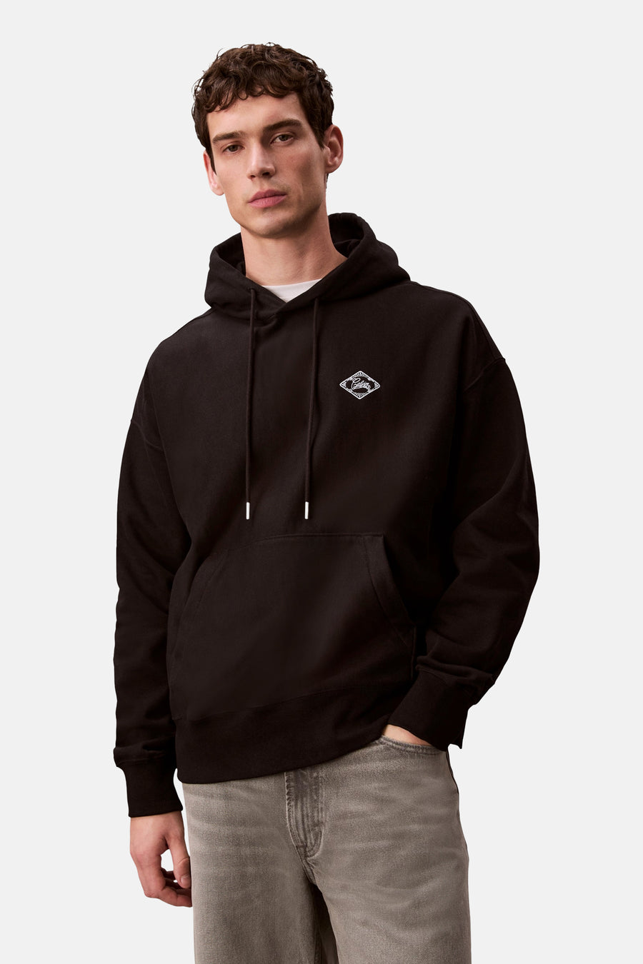 Sweat à capuche noir de Calvin Klein, avec cordon de serrage et logo discret sur la poitrine, porté avec un jean gris.
