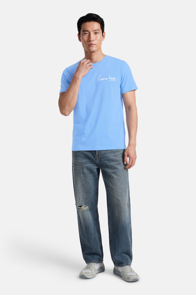 T-shirt bleu à manches courtes de Calvin Klein, porté avec un jean troué et des baskets.
