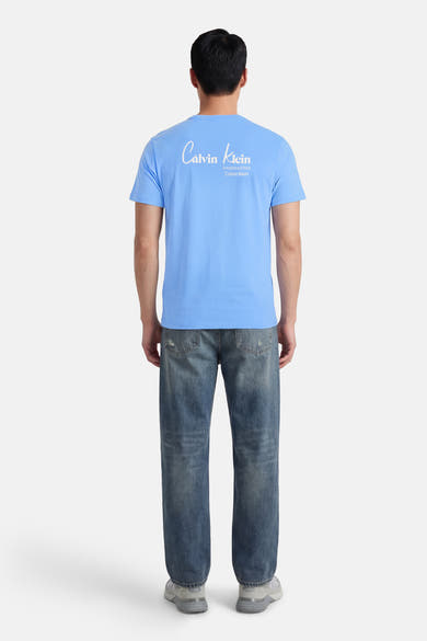 T-shirt à manches courtes bleu de Calvin Klein, avec logo imprimé au dos, porté avec un jean et des baskets.