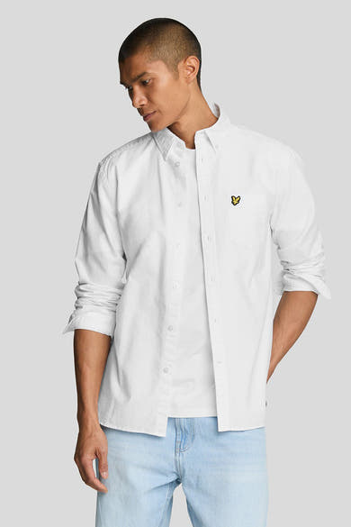 Chemise blanche à manches longues de LYLE & SCOTT, portée ouverte sur un t-shirt, avec un jean délavé.
