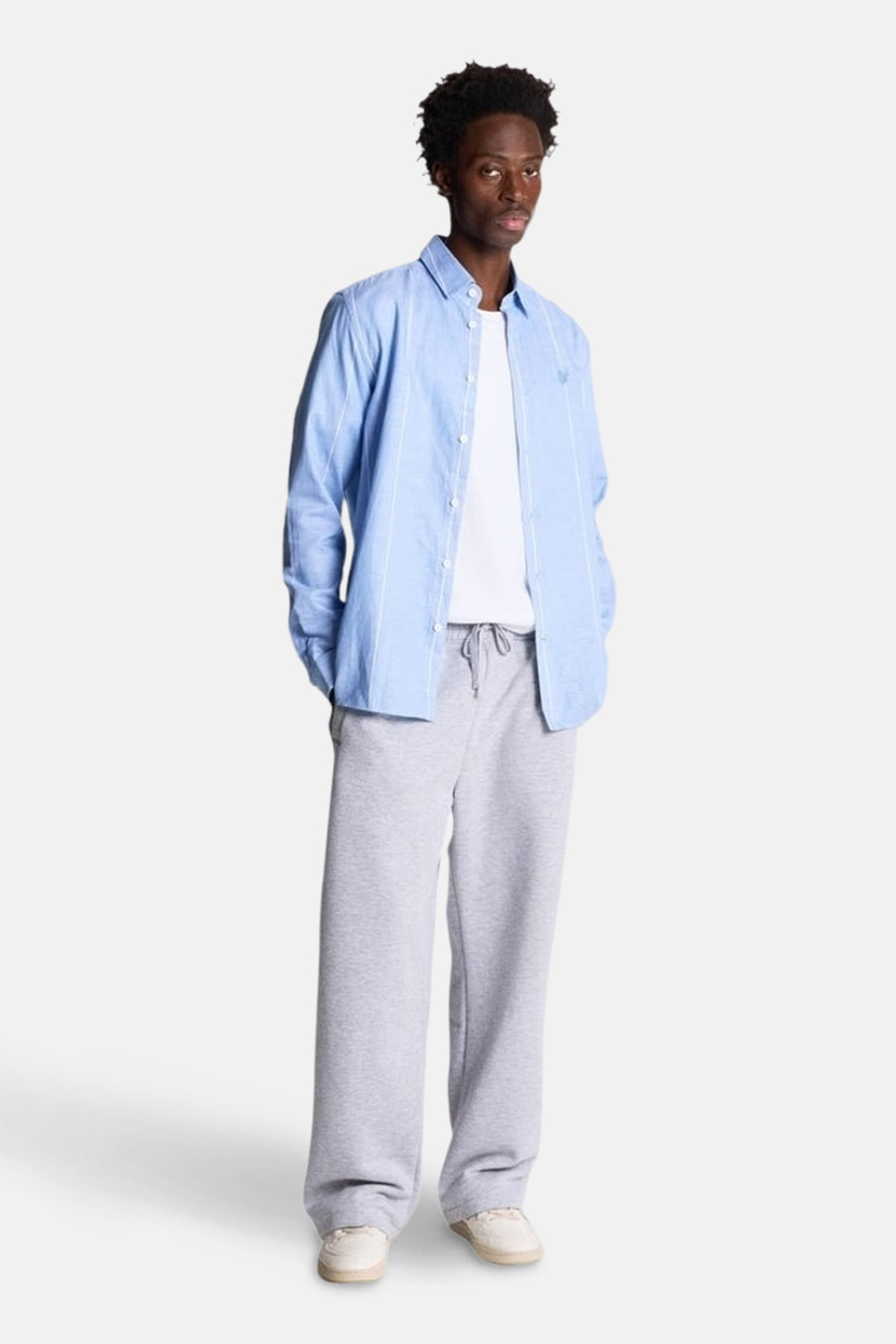 Chemise bleue à manches longues de LYLE & SCOTT, portée ouverte sur un t-shirt blanc et un pantalon de survêtement gris.
