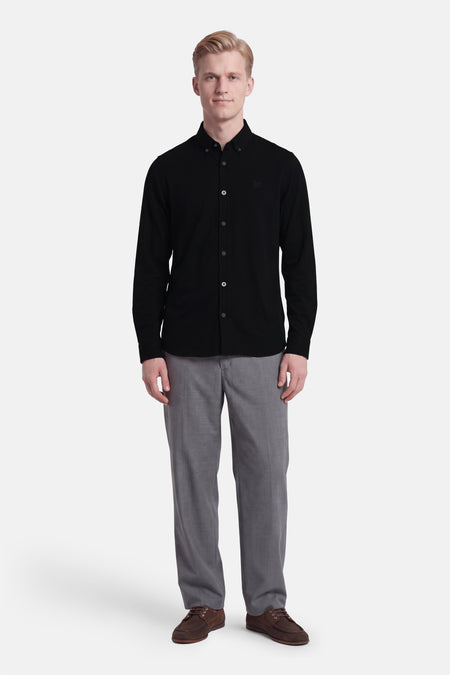 Chemise noire à manches longues par LYLE & SCOTT, boutonnée, avec logo discret sur poitrine, vue de face sur modèle en pantalon gris et chaussures marron