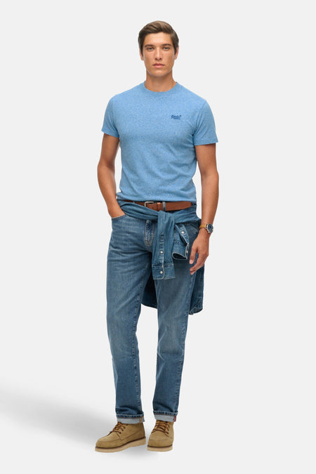 T-shirt bleu à manches courtes de SUPERDRY, porté avec un jean, une chemise en denim nouée et des chaussures marron.

