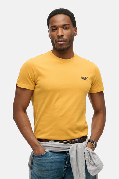 T-shirt ocre à manches courtes de Superdry, porté avec un jean et une chemise rayée nouée à la taille.