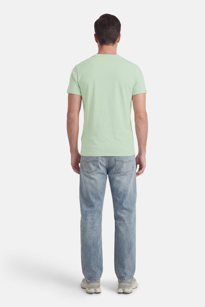 Groen T-shirt met korte mouwen van SUPERDRY, gedragen met een blauwe spijkerbroek en grijze sportschoenen, achtergezicht.