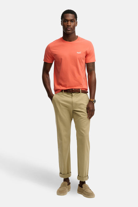 T-shirt corail à manches courtes de SUPERDRY, porté avec un pantalon chino beige, une ceinture tressée marron et des mocassins en daim.

