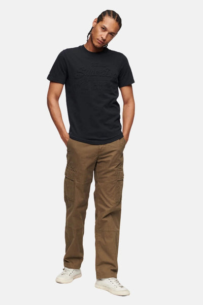 T-shirt bleu à manches courtes de SUPERDRY, avec un motif en relief sur le devant, porté avec un pantalon cargo marron.
