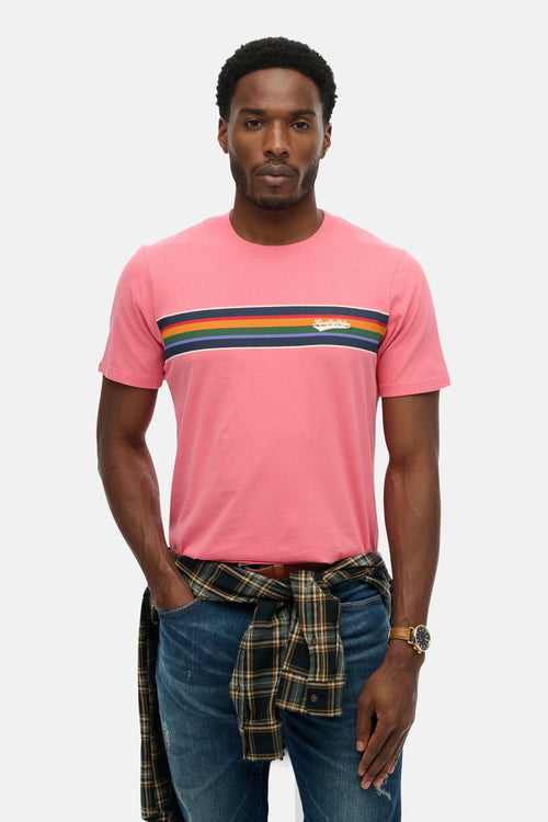 T-shirt à manches courtes rose de SUPERDRY avec rayures colorées sur la poitrine, porté avec une chemise à carreaux autour de la taille.