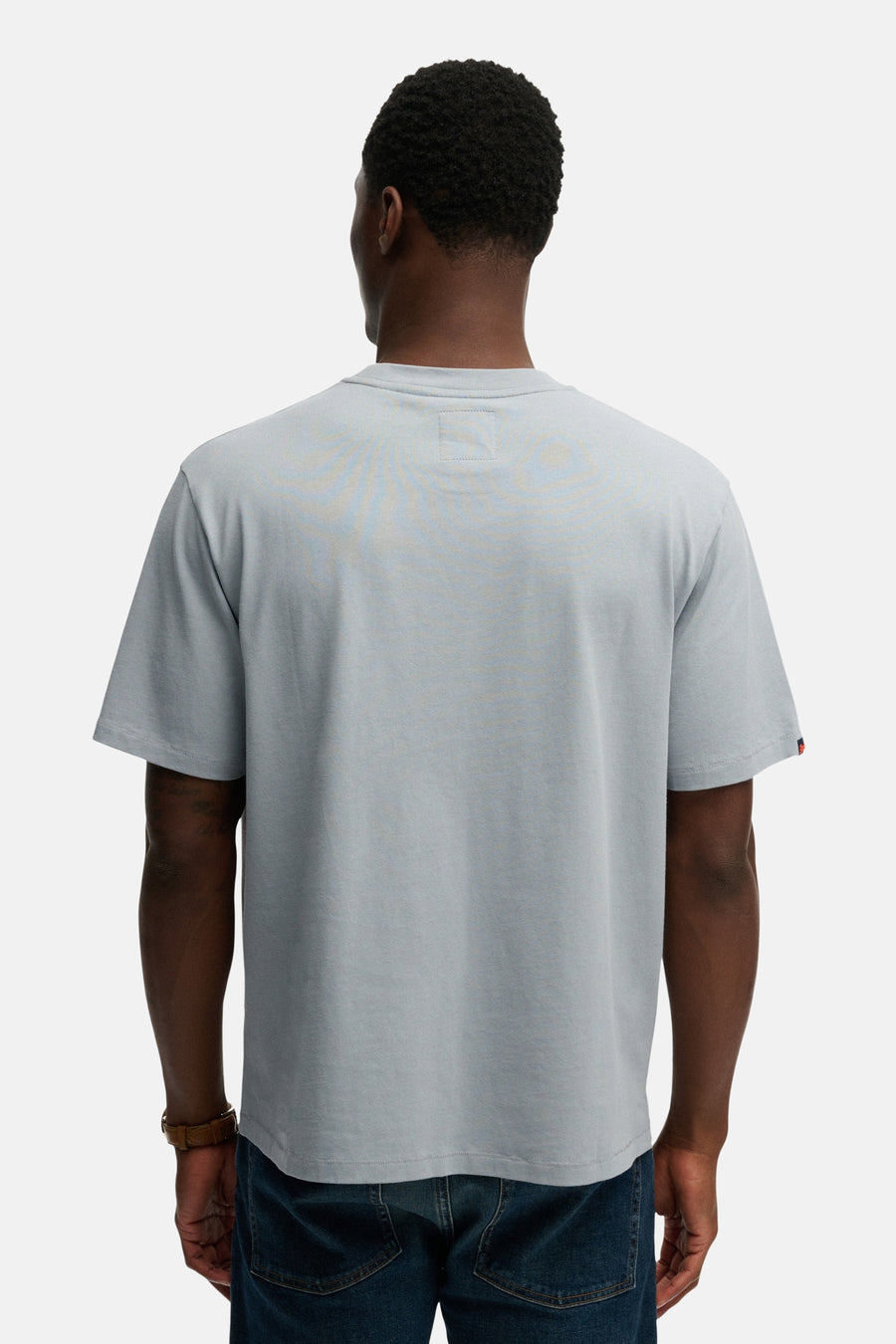 Blauw T-shirt met korte mouwen van SUPERDRY, met een rode zoom op de mouw en gedragen met een bruine armband en een blauwe spijkerbroek.