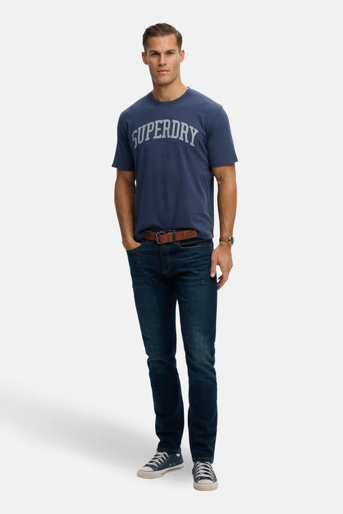 T-shirt à manches courtes bleu par SUPERDRY, porté avec un jean et des baskets en toile.