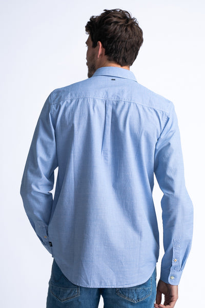 Chemise à manches longues bleue par Petrol Industries, avec pli creux au dos, portée avec un jean.