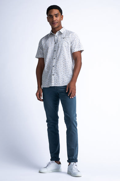 Chemise à manches courtes blanche à motifs, de Petrol Industries®, portée avec un pantalon bleu et des baskets blanches.