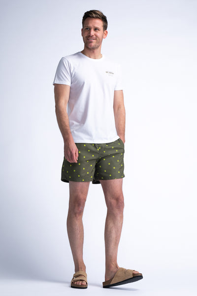 Short de bain vert à motifs de pattes, de Petrol Industries®, porté avec un t-shirt blanc uni et des sandales en cuir.