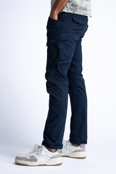 Blauwe cargobroek van Petrol Industries, met klepzakken en gedragen met witte sneakers.