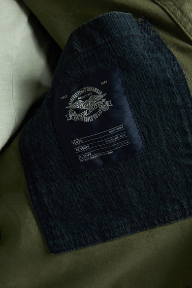 Kaki regenjas van Petrol Industries, met donker denim logo-label en zichtbare stikseldetails.