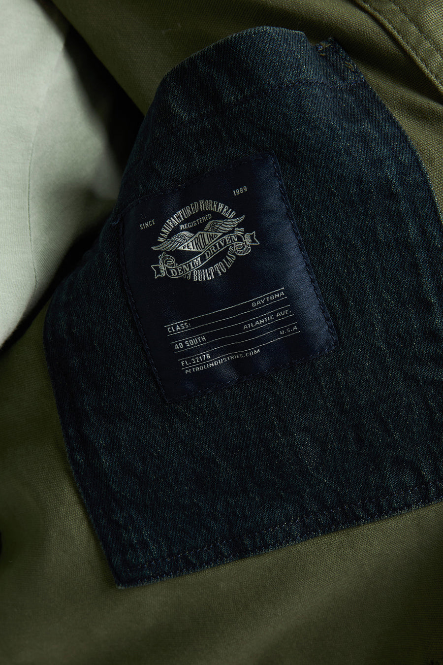 Kaki regenjas van Petrol Industries, met donker denim logo-label en zichtbare stikseldetails.