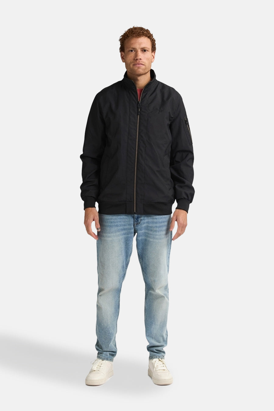 Zwarte jas van Petrol Industries, met ritssluiting en gedragen met een verbleekte spijkerbroek en witte sneakers.