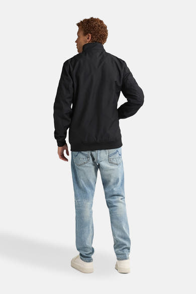 Zwarte jas van Petrol Industries, gedragen met een lichtblauwe jeans en gebroken witte sneakers, van achteren gezien.