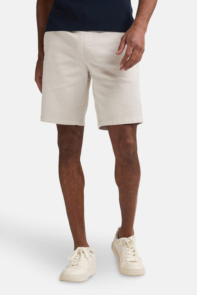Korte beige short van Petrol Industries, gedragen met een marineblauw T-shirt en witte sneakers.