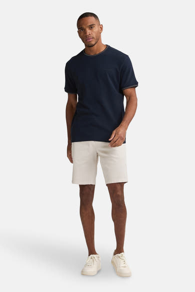 Korte beige short van Petrol Industries, gedragen met een marineblauw T-shirt en witte sneakers.
