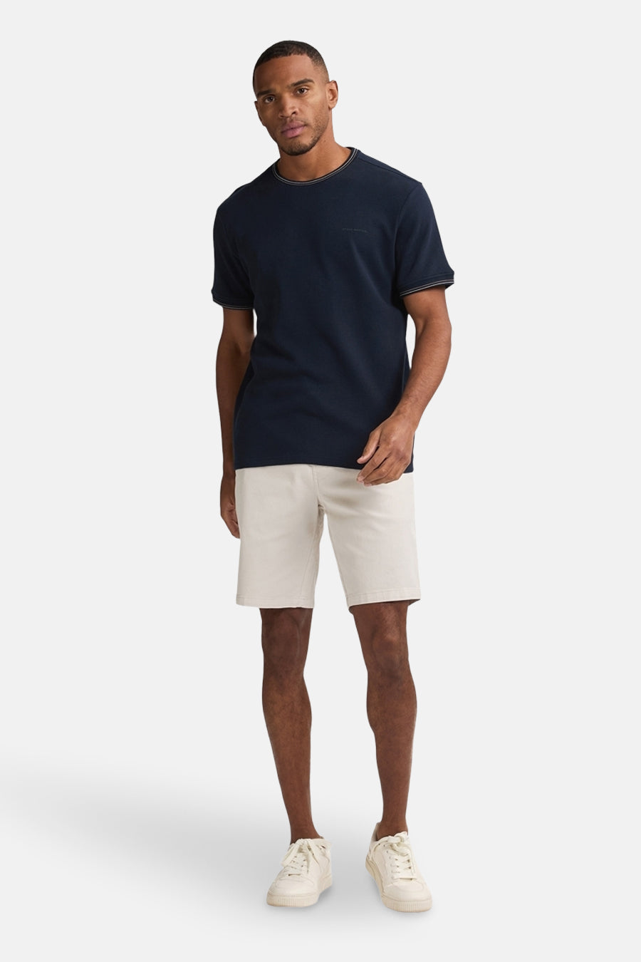 Korte beige short van Petrol Industries, gedragen met een marineblauw T-shirt en witte sneakers.