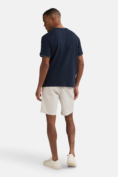 Korte beige short van Petrol Industries, gedragen met een marineblauw T-shirt en bijpassende sneakers, van achteren gezien.
