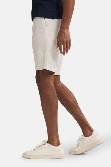 Korte beige short van Petrol Industries, gedragen met een marineblauw T-shirt en witte sneakers.