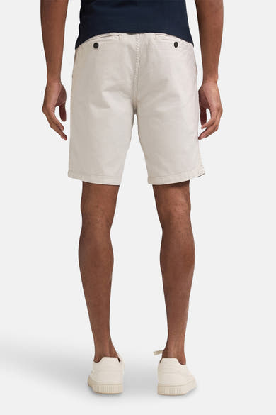 Korte beige van Petrol Industries, met achterzakken met knopen, gedragen met een marineblauw T-shirt en crèmekleurige sneakers.