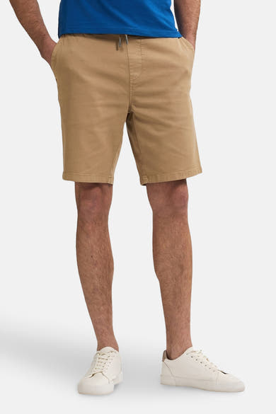 Korte beige short van Petrol Industries, gedragen met een blauw T-shirt en witte sneakers.