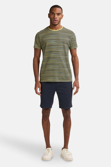 Korte blauwe spijkerbroek van Petrol Industries, gedragen met een gestreept T-shirt en witte schoenen.