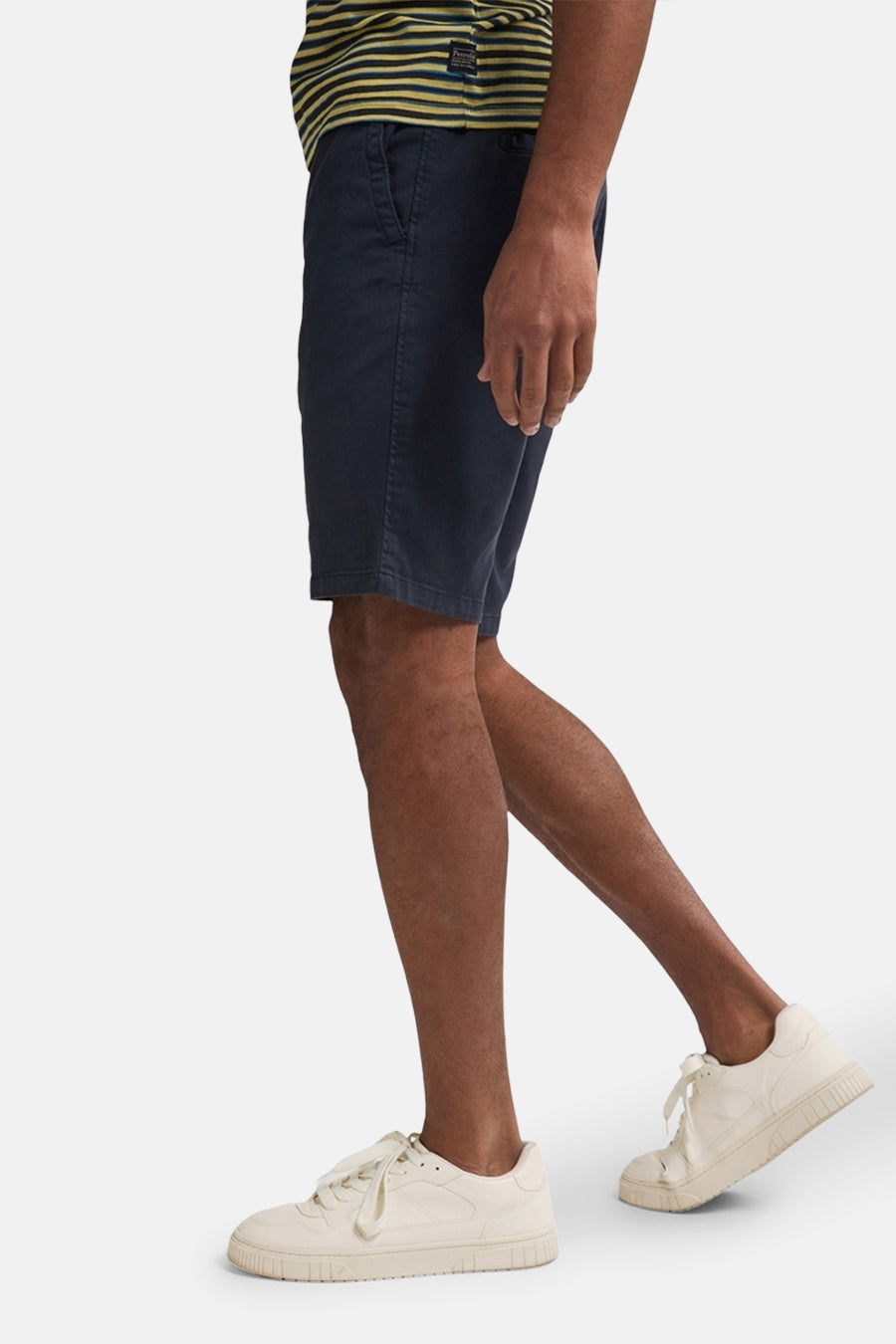 Korte blauwe spijkerbroek van Petrol Industries, gedragen met een gestreept T-shirt en beige sneakers, zijaanzicht.