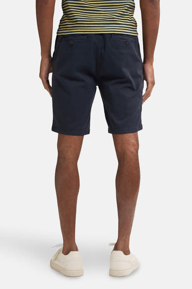 Korte blauwe jas van Petrol Industries gedragen met een gestreept T-shirt en witte sneakers, achtergezien.