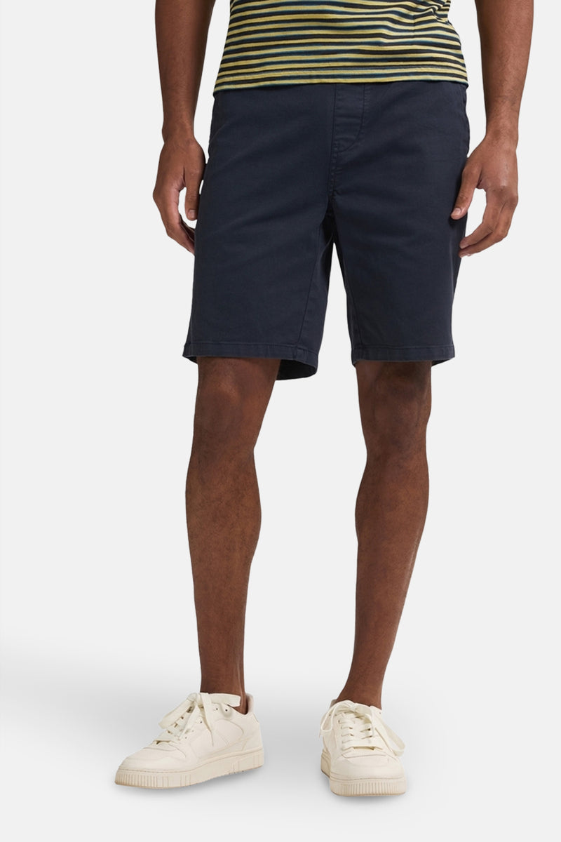 Korte blauwe broek van Petrol Industries, gedragen met een gestreept T-shirt en witte sportschoenen.
