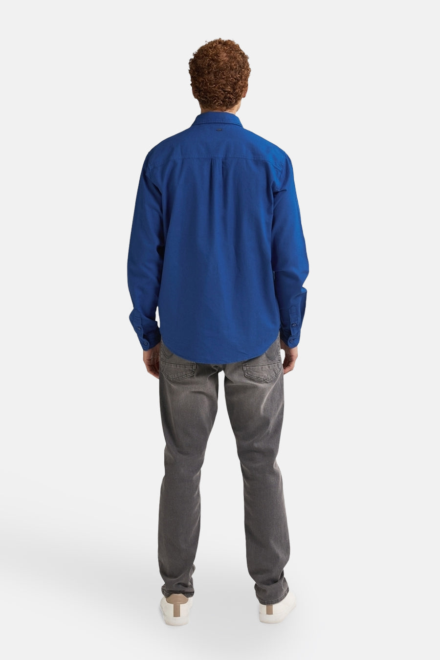 Chemise à manches longues bleue de Petrol Industries, vue de dos, portée avec un jean gris et des baskets blanches.