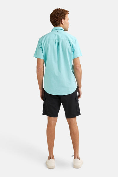 Chemise turquoise à manches courtes de Petrol Industries, vue de dos, portée avec un short cargo noir et des baskets blanches.