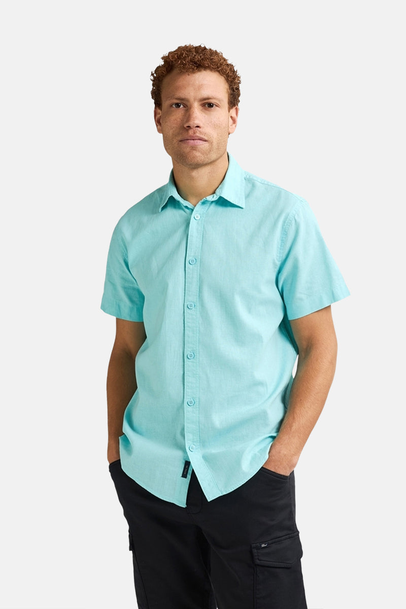 Chemise turquoise à manches courtes de Petrol Industries®, avec des boutons et portée avec un pantalon noir.