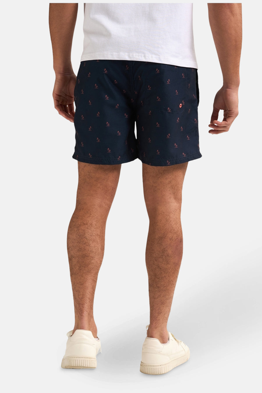 Short de bain bleu foncé de Petrol Industries®, à motif de palmiers rouges, porté avec un t-shirt blanc et des chaussures blanches.